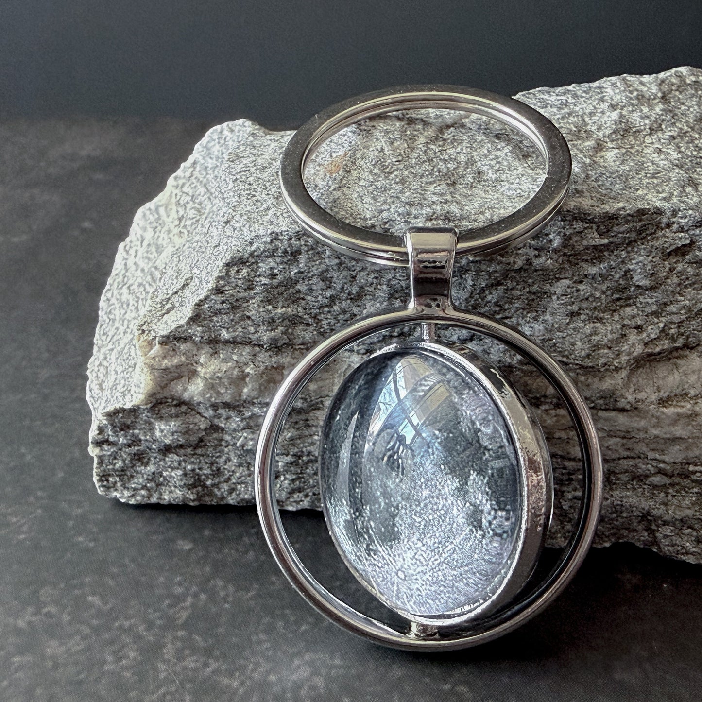 Silver keychain with a circular design on a rock background