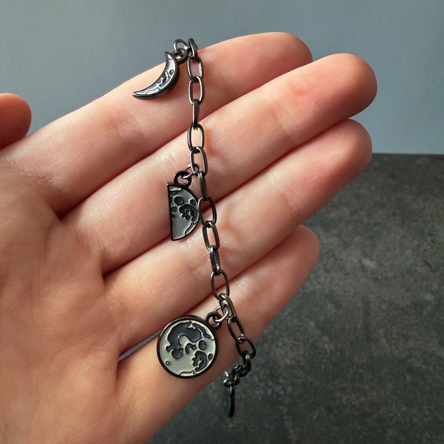 Hand holding a bracelet with Moon Phase charms against a neutral background