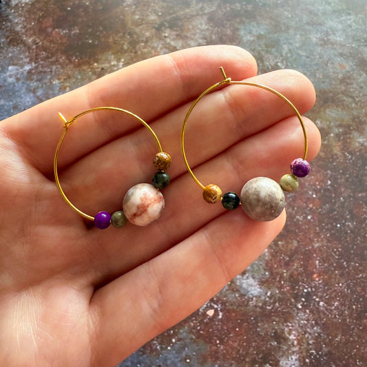 Gold hoops with 1 large bead representing Jupiter and 4 smaller beads representing Jupiter's moons, being help in a hand. 