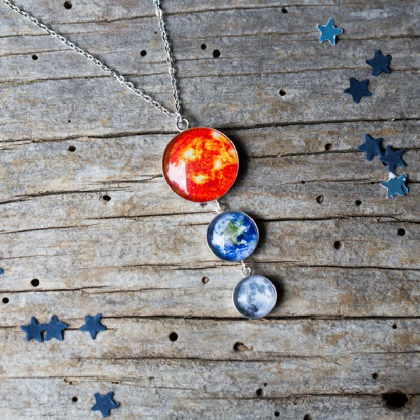 Necklace with Sun, Earth and Moon images on a wooden background with blue star confetti.
