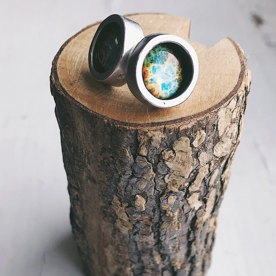 Silver-toned Stud earrings with nebula image design resting on a rustic wood log. 