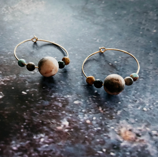 A pair of silver hoop earrings with large natural stone beads and smaller accent beads, displayed on a dark textured surface.