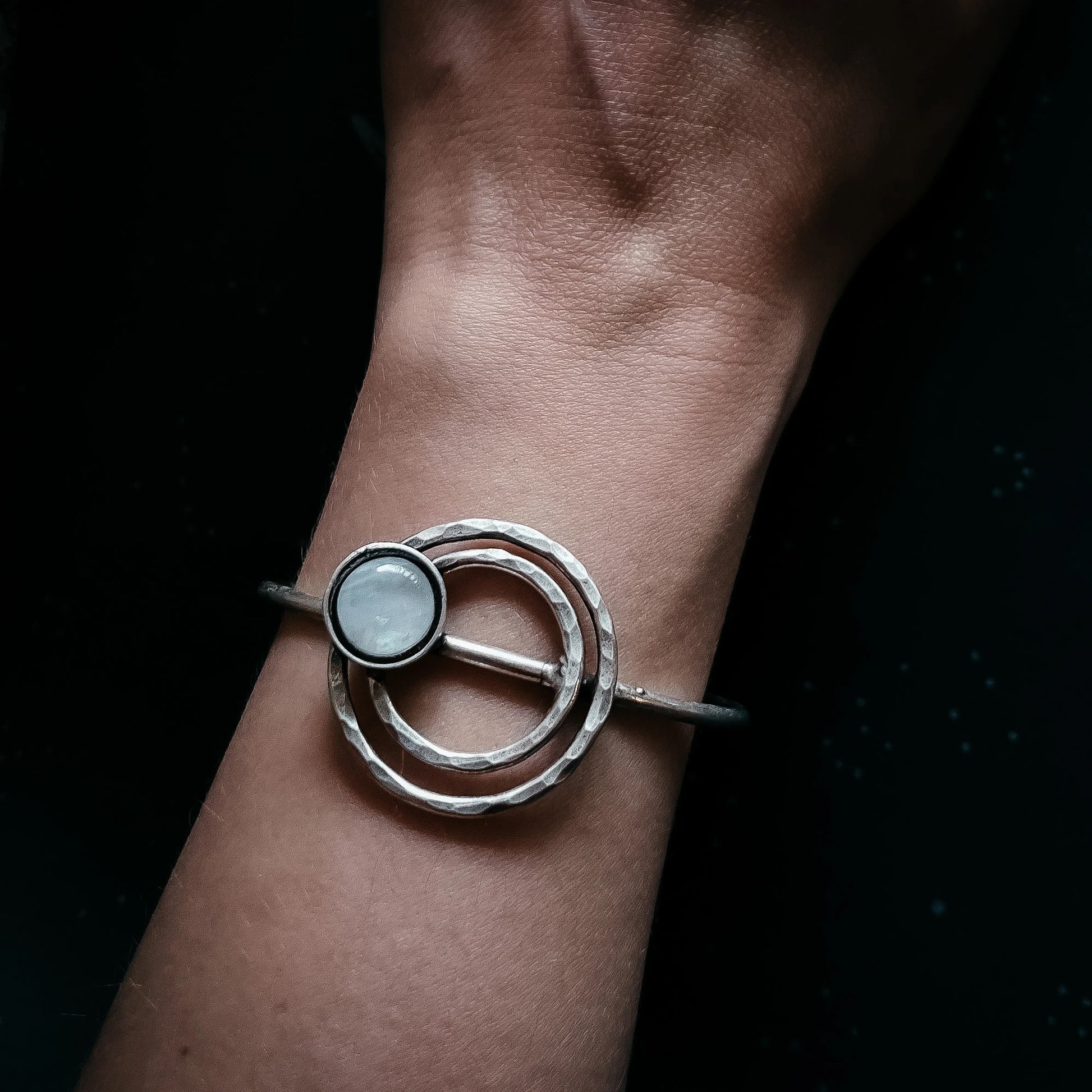 A silver-toned textured ring bangle with a circular white inlay, shown worn on a person's wrist against a dark background.