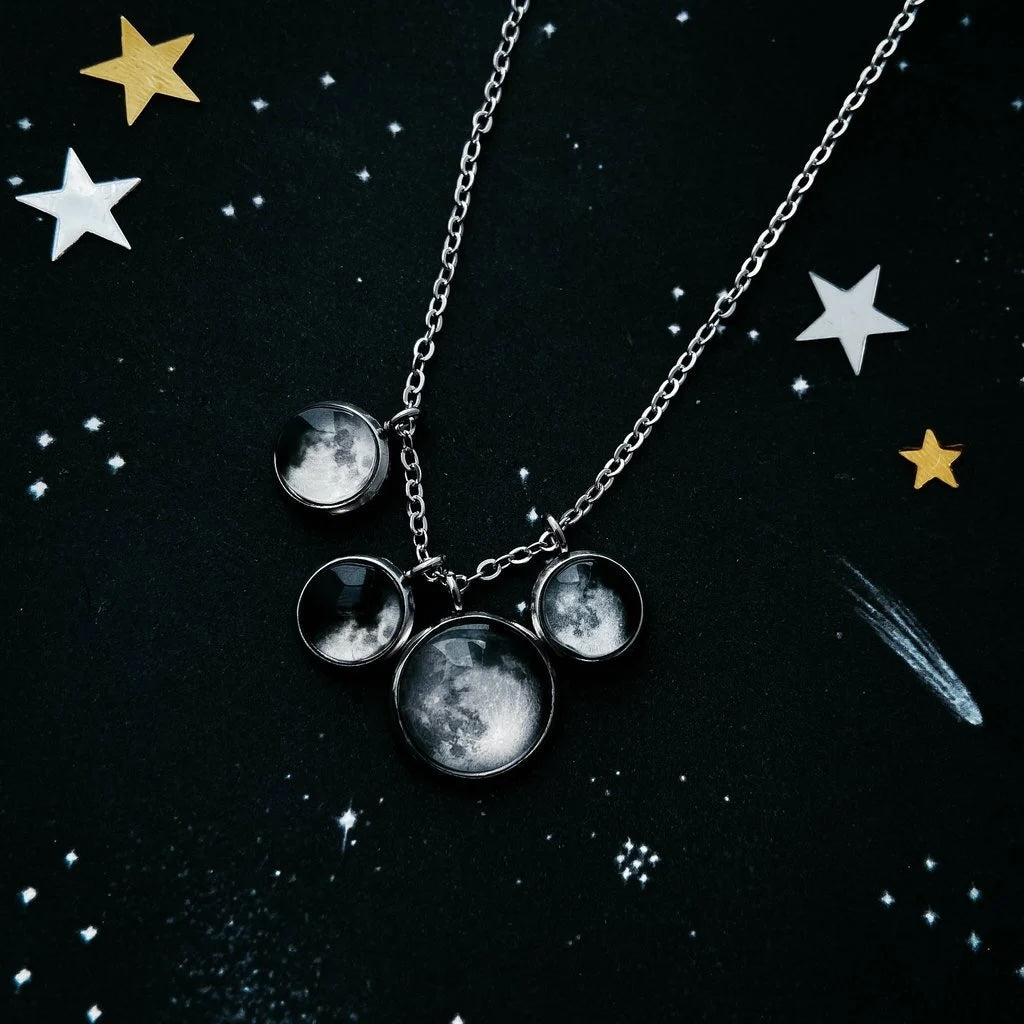 A silver chain necklace with moon phase charms hanging off of it,  displayed on a dark starry background.
