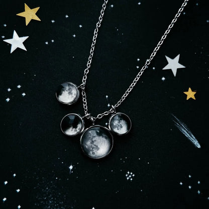 A silver chain necklace with moon phase charms hanging off of it,  displayed on a dark starry background.