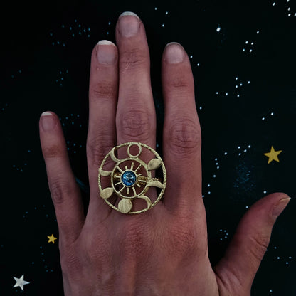 Hand wearing a gold ring with an earth image at the center against a starry night sky background