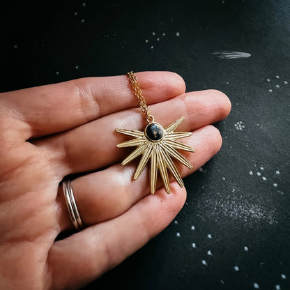 Gold sun-shaped pendant held in a hand against a dark background